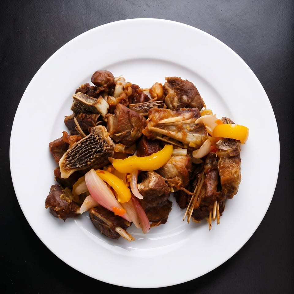 A white plate filled with stewed meat, yellow bell peppers, and red onions on a dark surface.