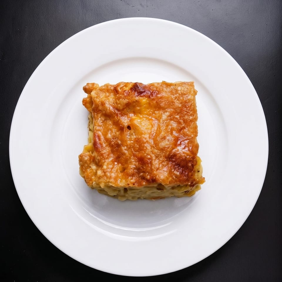 Golden-brown baked macaroni and cheese square on a white plate against a dark background.
