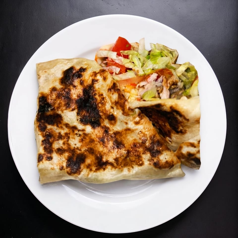 Grilled flatbread wrap with chicken, lettuce, and tomato, served on a white plate.
