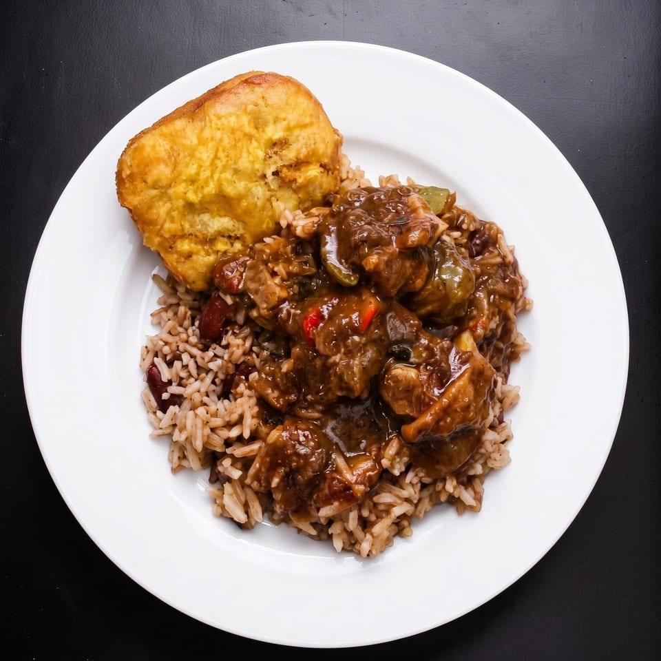 Brown stew chicken with rice and peas, and a fried dumpling on a white plate.